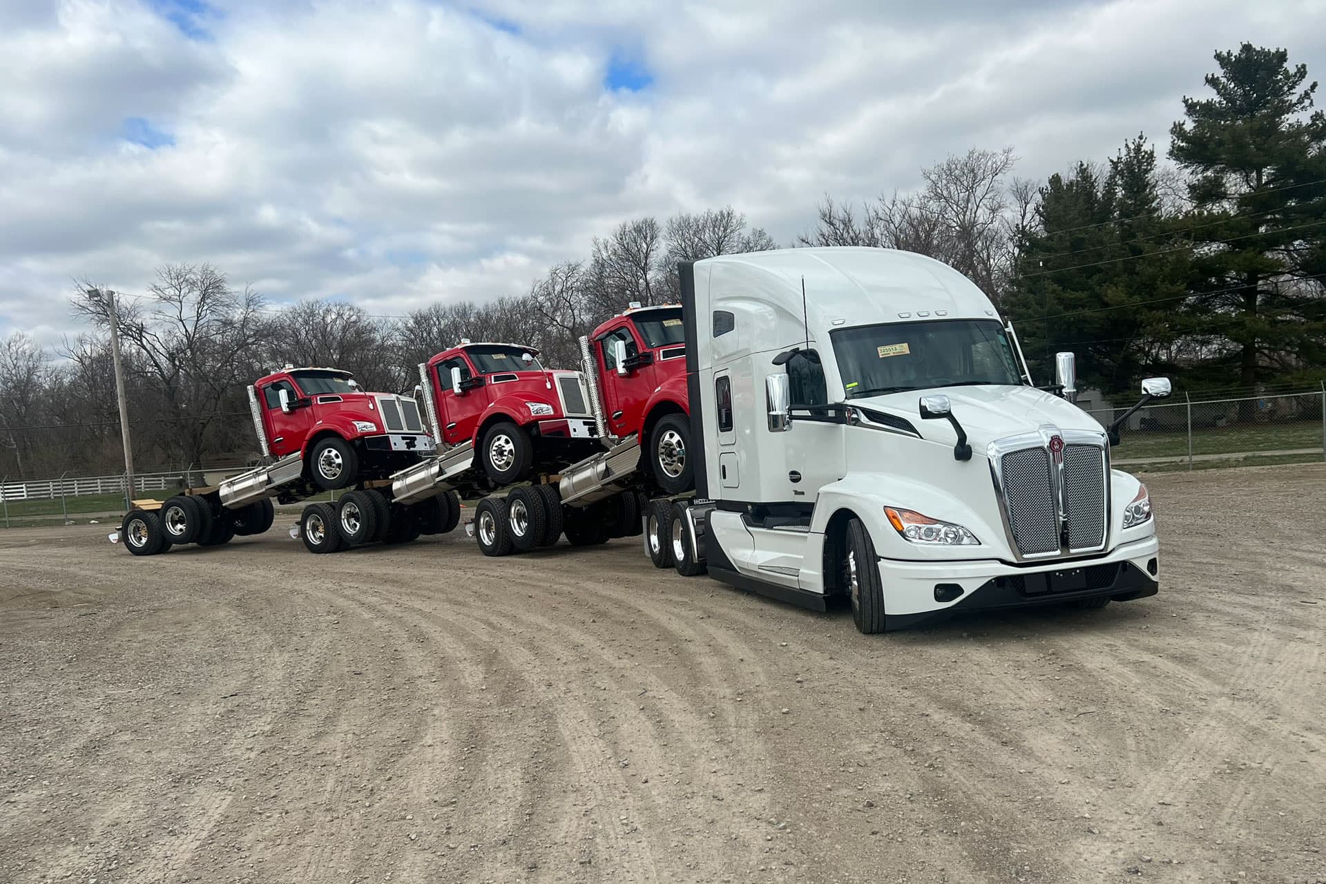 A white truck pulling three red trucks
